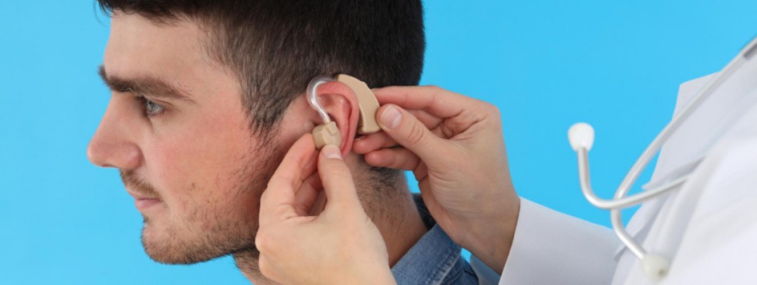 Γιατρός δείχνει σε νεαρό άντρα πώς λειτουργούν τα ακουστικά βαρηκοΐας, τοποθετώντας τα στα αυτιά του.